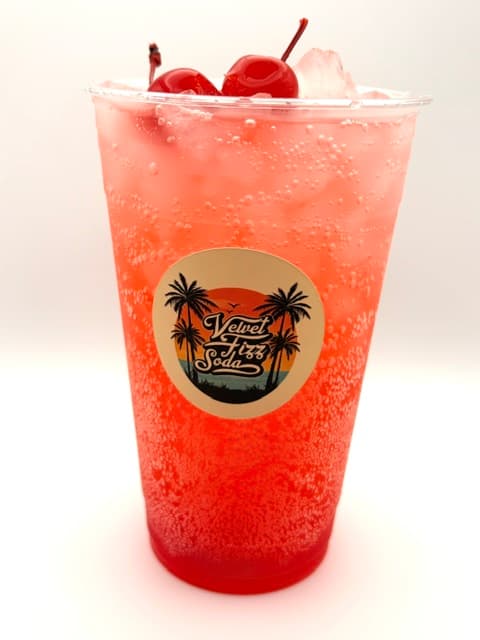 Bubbly pink soda with ice and maraschino cherries in a Velvet Fizz Soda cup.