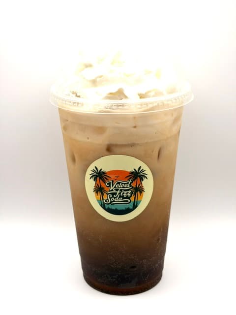 Layered dark soda and cream beverage topped with whipped cream in a Velvet Fizz cup.