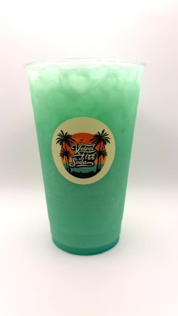 Frothy light green soda in a plastic cup featuring a tropical Velvet Fizz Soda logo.
