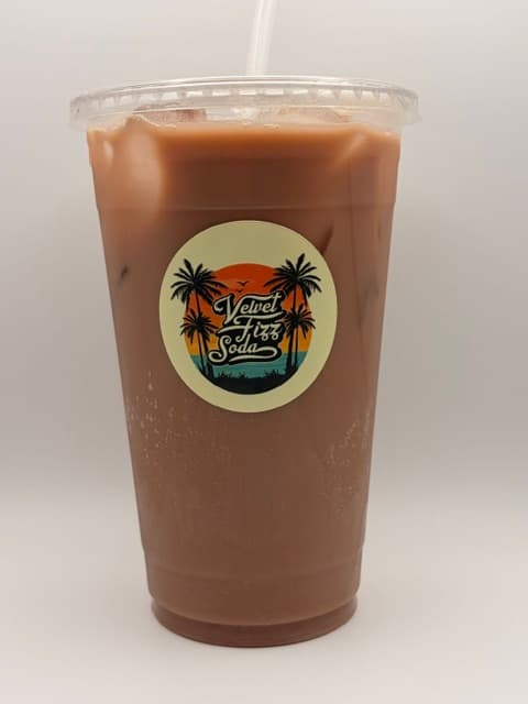 Clear plastic cup of iced brown soda with a Velvet Fizz Soda tropical sticker.